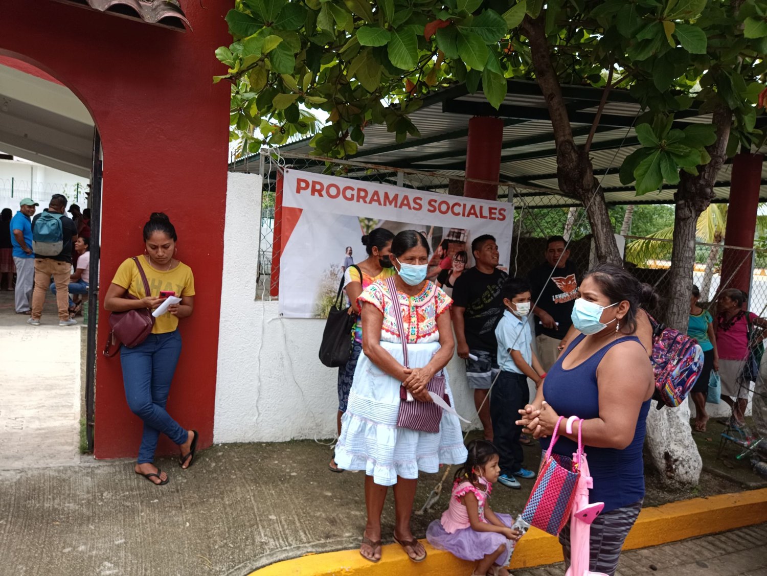 Familias reunidas junto a un cartel de programas sociales en San Pedro Mixtepec, Oaxaca, 2022